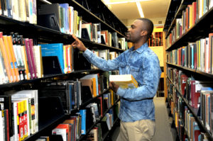 Male student holding a book and picking out more books from the library