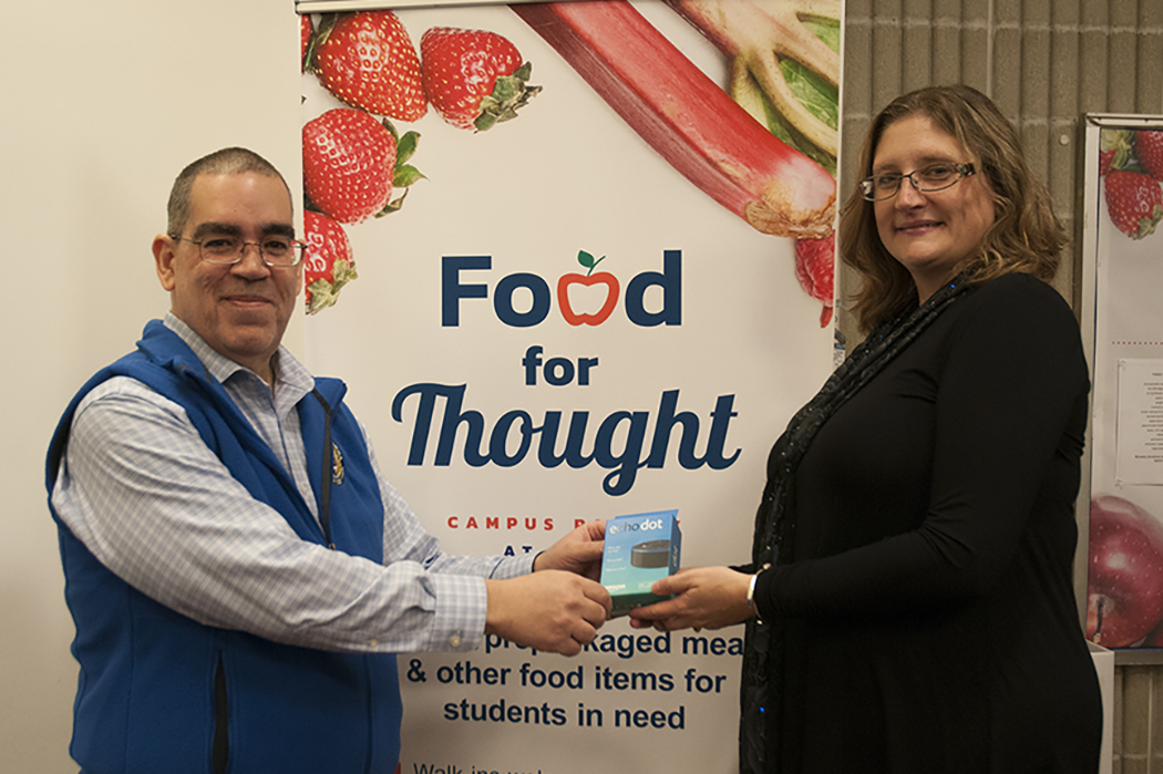 MWCC Assistant Professor of Business Geraldo Maldonado stands with Director of the Senator Stephen M. Brewer Center for Civic Learning Shelley Nicholson holding the Echo Dot Maldonado won as part of the Do One Thing campaign.