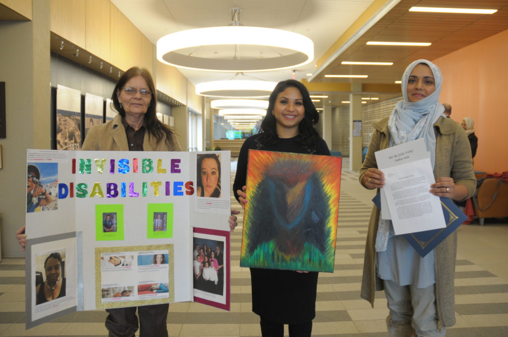 Three women stand in a row holding their projects in front of them.