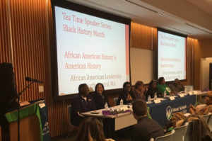 Six panelists sit in front of an audience.