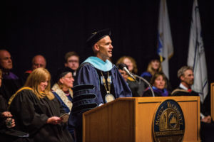 MWCC President Vander Hooven stands in front of a lecturn giving a speech while wearing academic regalia.