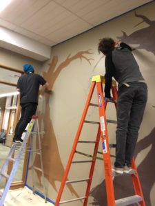 Two art students on ladders beginning to paint tree trunks