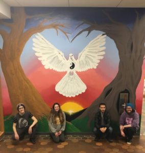 Four student artists crouch in front of a colorful mural they created