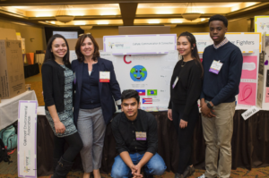 Champion standing next to Culture, Communication, & Connection Venture Team in front of their tri-fold board