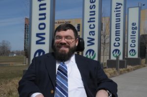 Nate Johnson sits in front of signs outside of Mount Wachusett Community College.