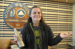 A woman holds up a container of grains in one hand and dog treats in the other.