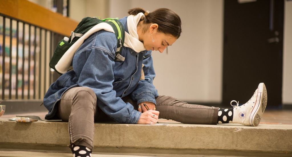 Female student writing while sitting on steps