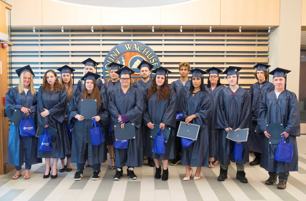 Two rows of students in graduation cap and gowns line up for a photo.