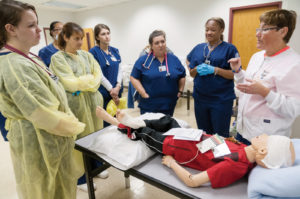 A group of nursing students and an instructor gather around a mannequin during a nursing class.