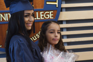 A woman in a graduation outfit poses with her daughter for a photo.