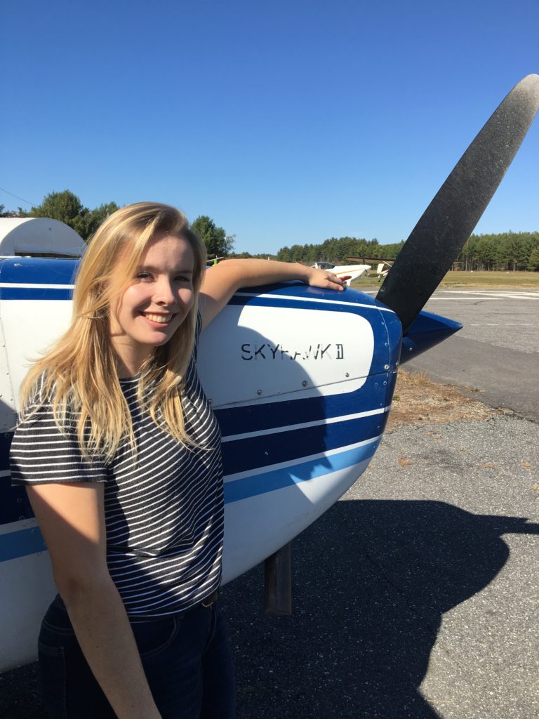 Cassie Standing resting her arm on a Plane propeller