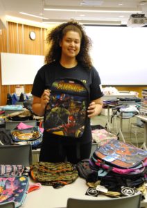 A college-age woman stands holding a child's backpack.