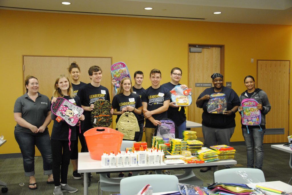 A group of students stands in a row holding children's backpacks.