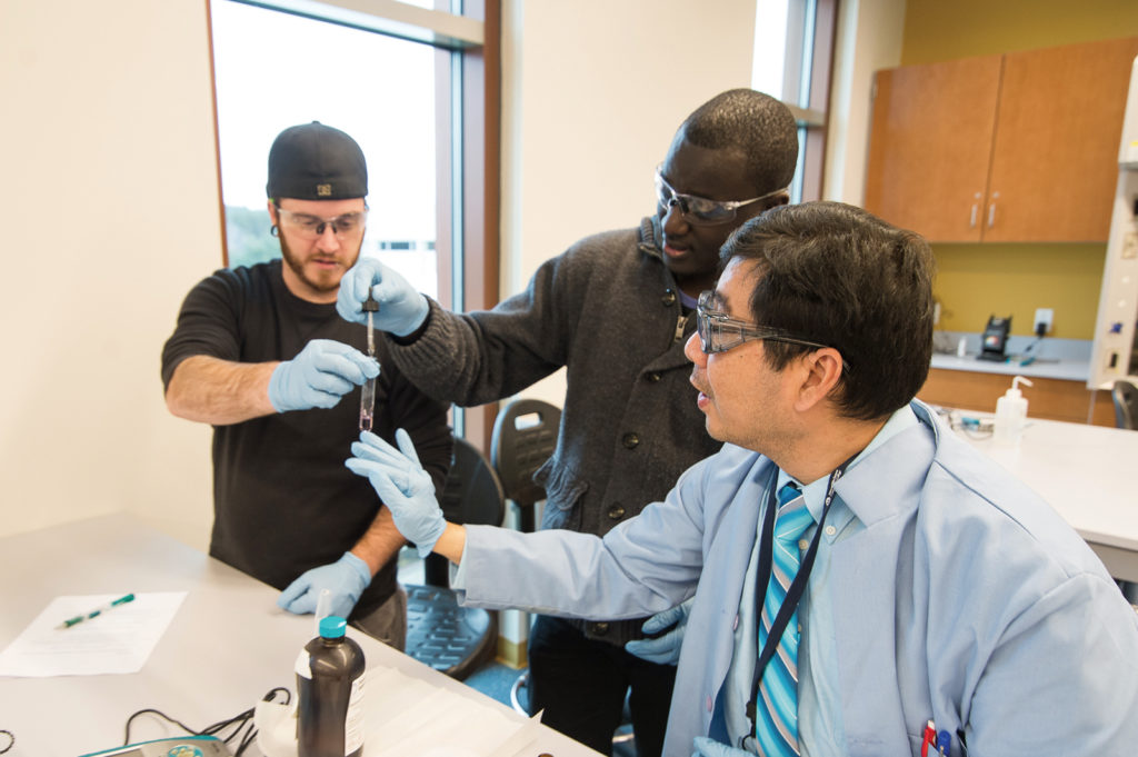 A professor instructs two students in a college science lab.