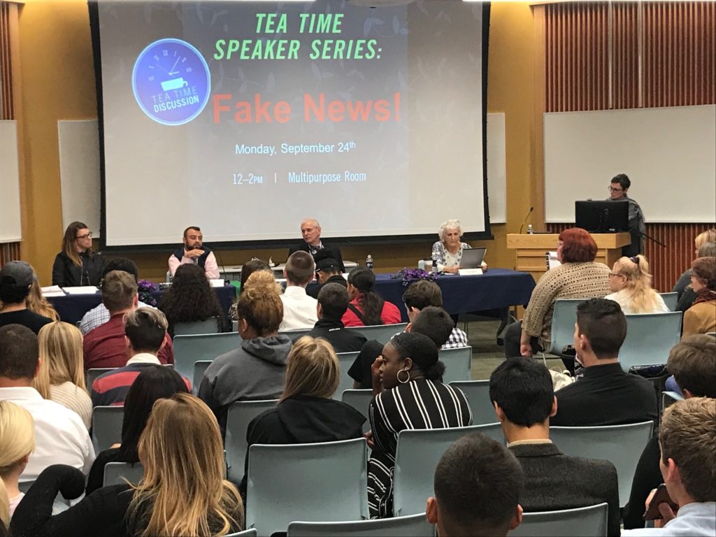 Four panelists sit at a table and speak to an audience of people.