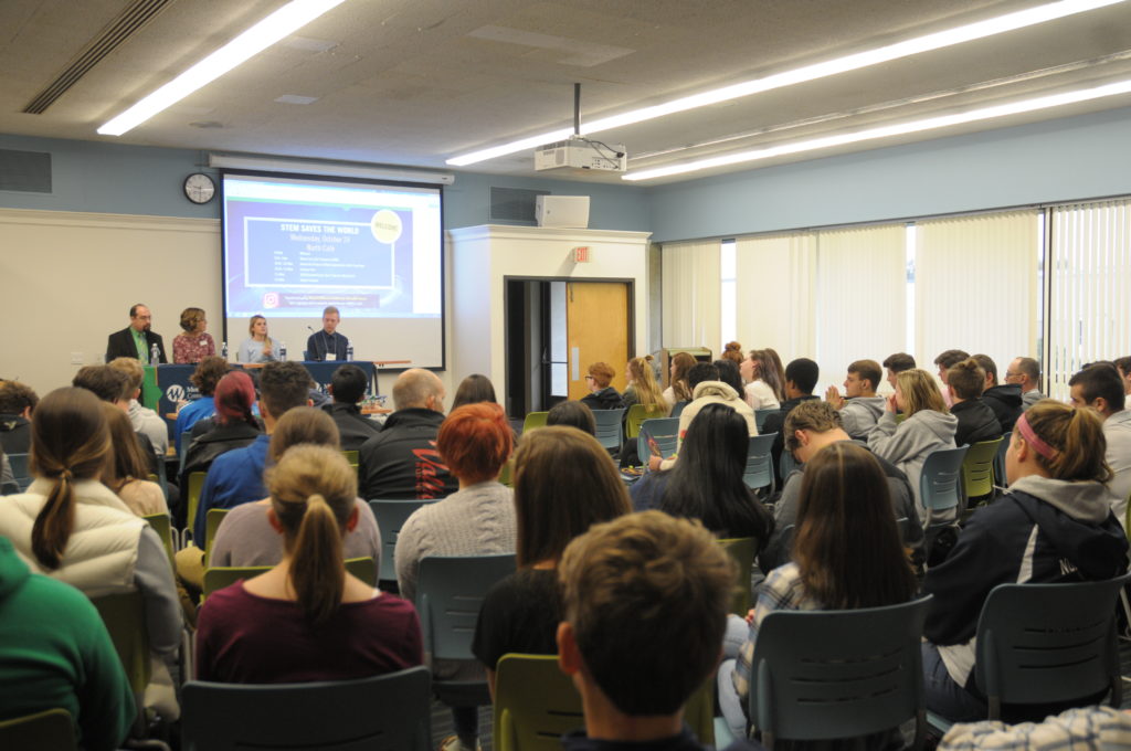 Four people sit in front of an audience.