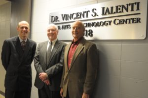 Three men stand in front of a sign.