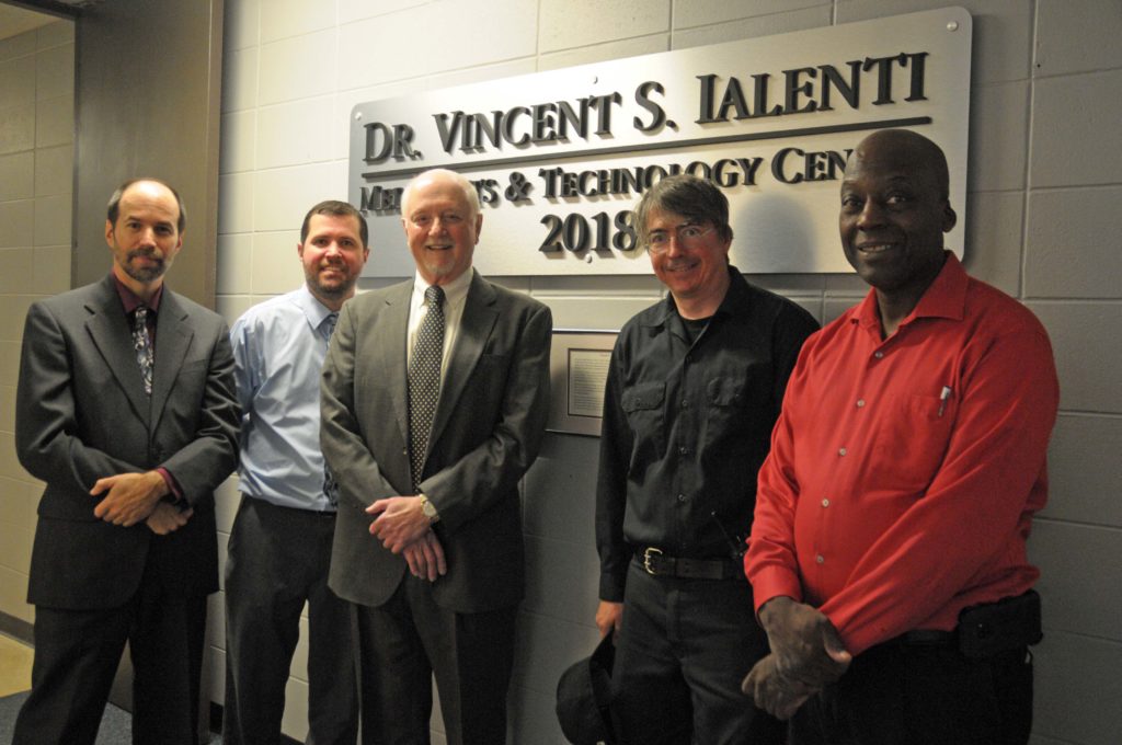 Five men stand in a row in front of a sign.