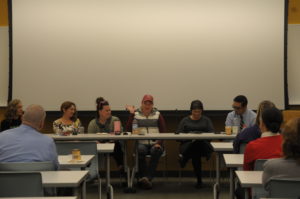 Six people sit in front of a group of people.