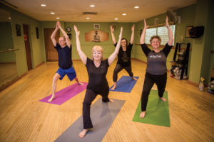 Four people do a yoga pose with their hands in the air.