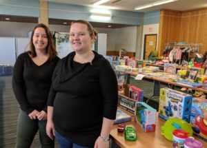 Two people stand in front of tables covered with toys.