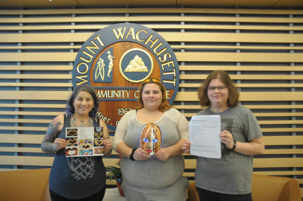 Three people stand in a row holding items in front of them.