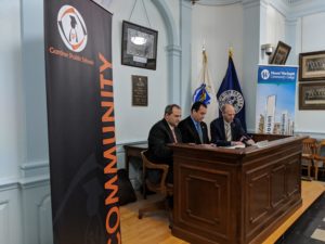 Three people sign a document while sitting at a desk.