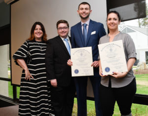 Four people stand in a line. Two hold large pieces of paper that are citations.