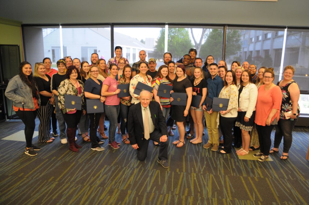 A man kneels in front of a large group of students posing for a photo.