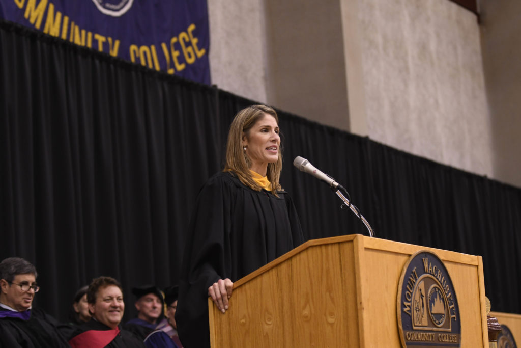 A woman stands at a podium addressing an audience.