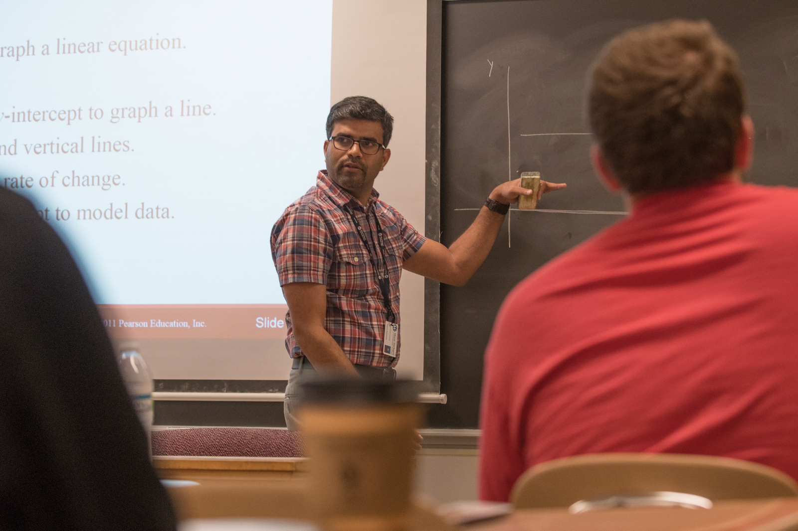 A professor stands in front of a blackboard teaching students.