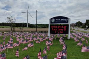 The grass is covered with American flags and a digital sign in the background gives information about the veteran's fair.