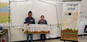 2 girls stand in front of a whiteboard holding a giant check