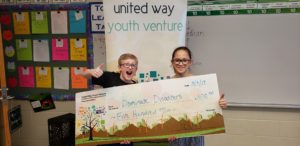 2 kids stand behind a giant check