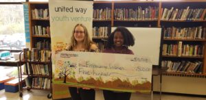 2 teens stand behind a giant check