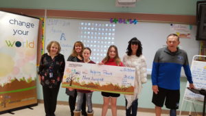 4 kids stand with a giant check with 2 adults