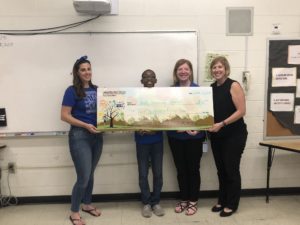 1 teen and 3 adults stand behind a giant check