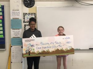 2 teens stand behind a giant check