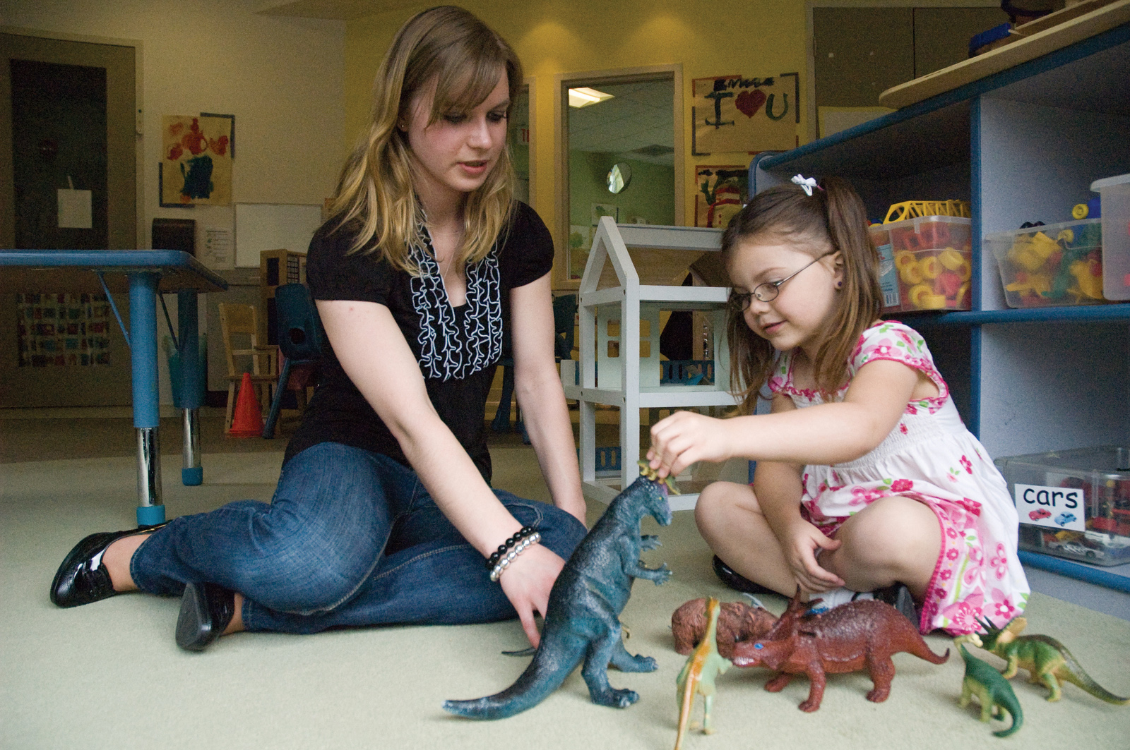 A woman interacts with a child who is playing with toy dinosaurs.