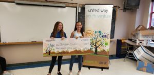 2 kids stand while holding a giant check