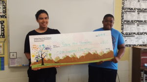 2 kids stand behind a giant check