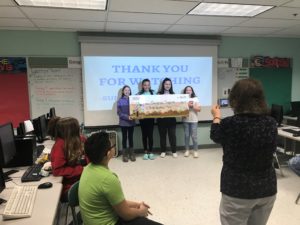 4 kids stand holding a giant check while a woman takes a picture of them