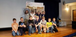 10 kids stand on stage while raising a giant check