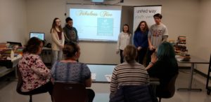 4 teens stand in front of 4 sitting adults, presenting a slideshow