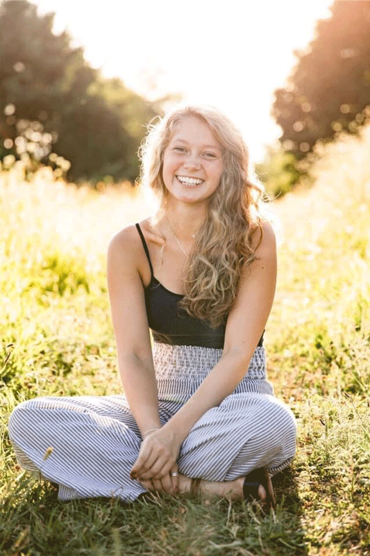 Student Olivia Wells sitting in field smiling