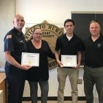 Four people hold up certificates.