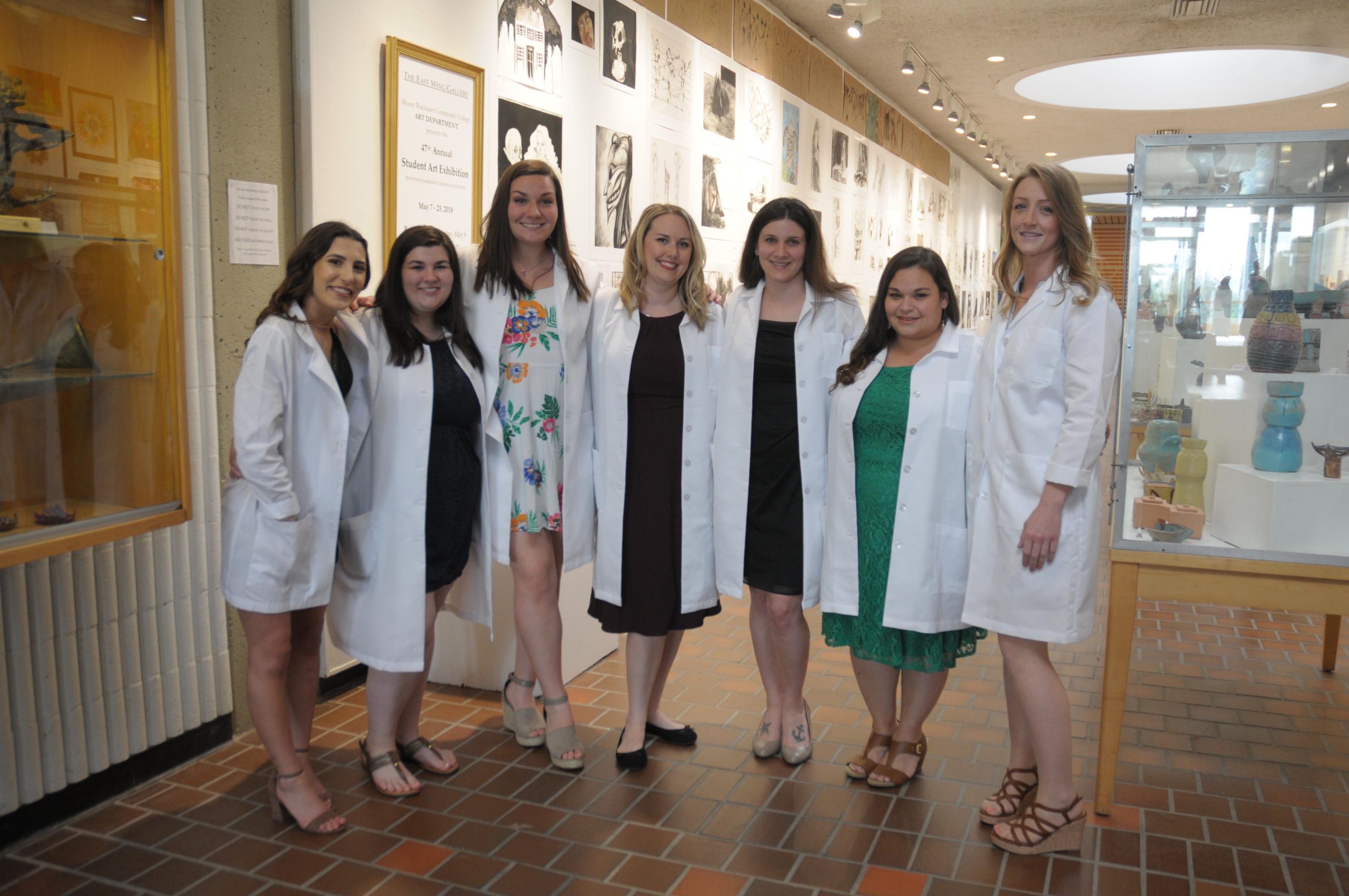 A group of women in dressed up clothing and white lab coats are lined up for a photo.
