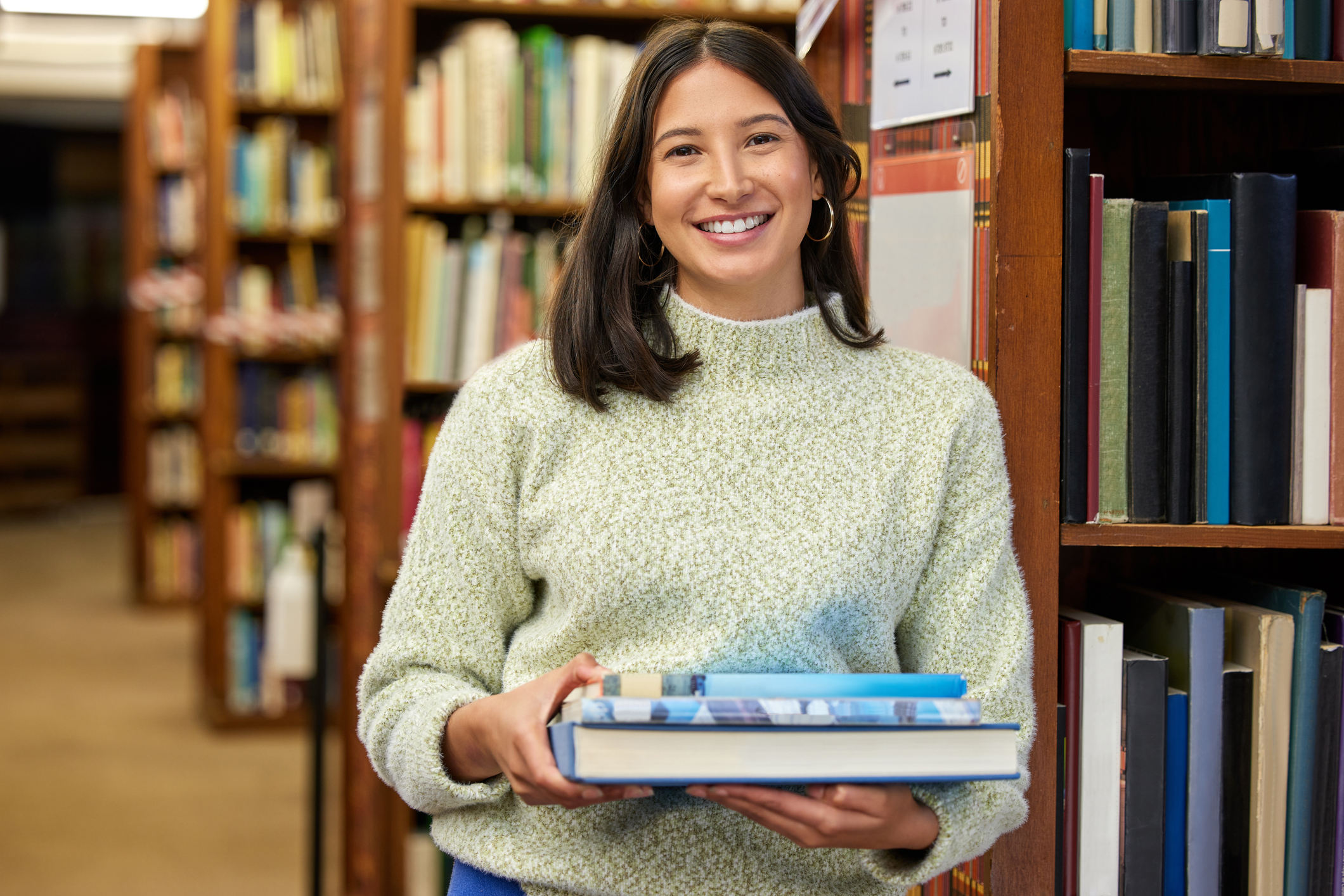Shot of a young woman holding books in a library