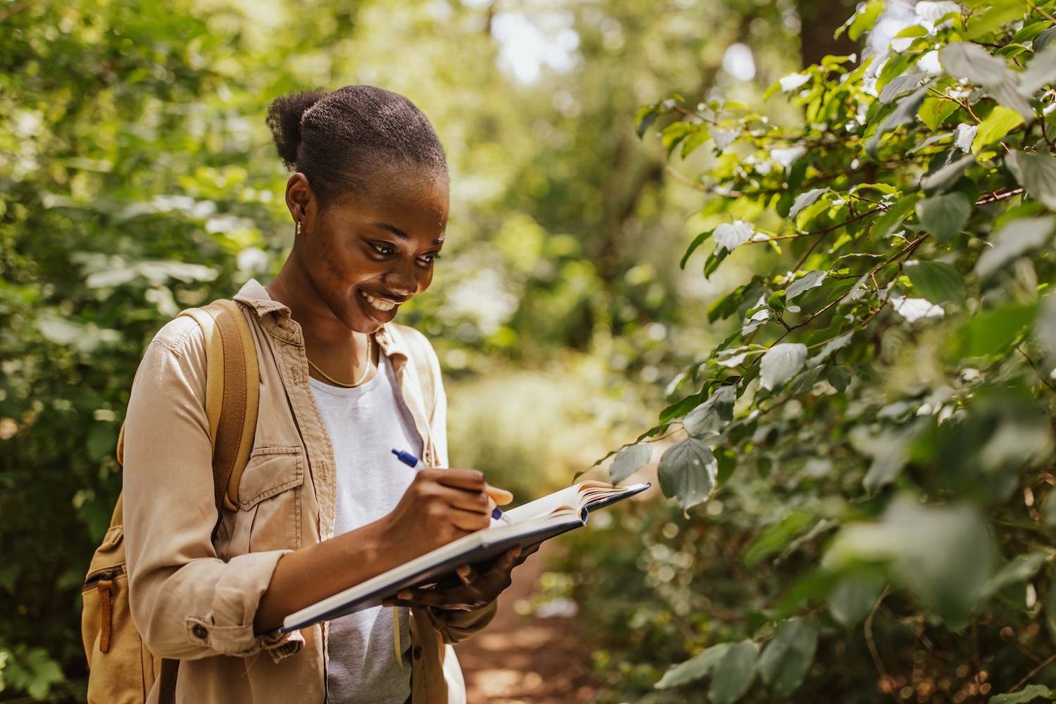 Person in forest taking notes from open book