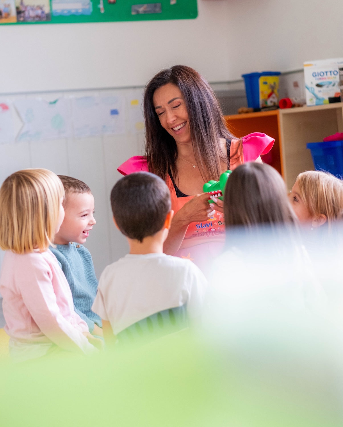the children have gathered in a circle with the teacher and she is showing them a game